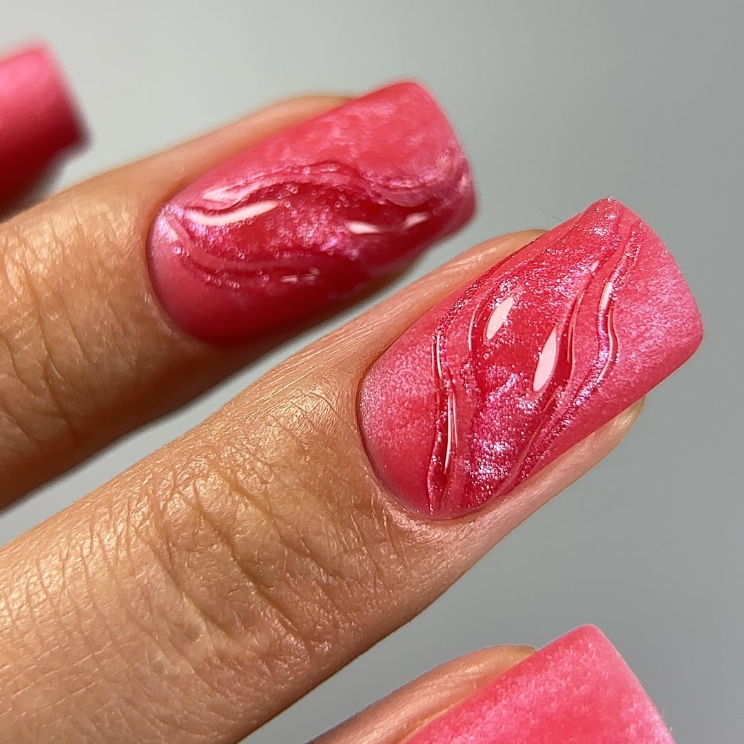 Close-up of nails painted with Paloma gel nail polish in shade C076, a vibrant red with a pink shimmering effect. The nail art features a unique textured design with a glossy and matte contrast, highlighting the rich, highly-pigmented color and long-lasting finish. Ideal for creating bold, eye-catching manicures with a touch of sparkle