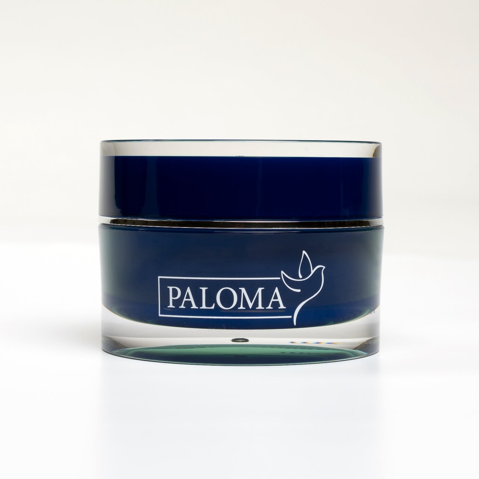 A frontal view of a refined, transparent jar topped with a deep blue lid, prominently featuring the name &#39;PALOMA&#39; in elegant white typography accompanied by a stylized dove logo. Inside the jar lies the renowned Paloma builder gel, designed for nail enhancements, showcased against a crisp, white backdrop that underscores the professional quality of the studio photograph.