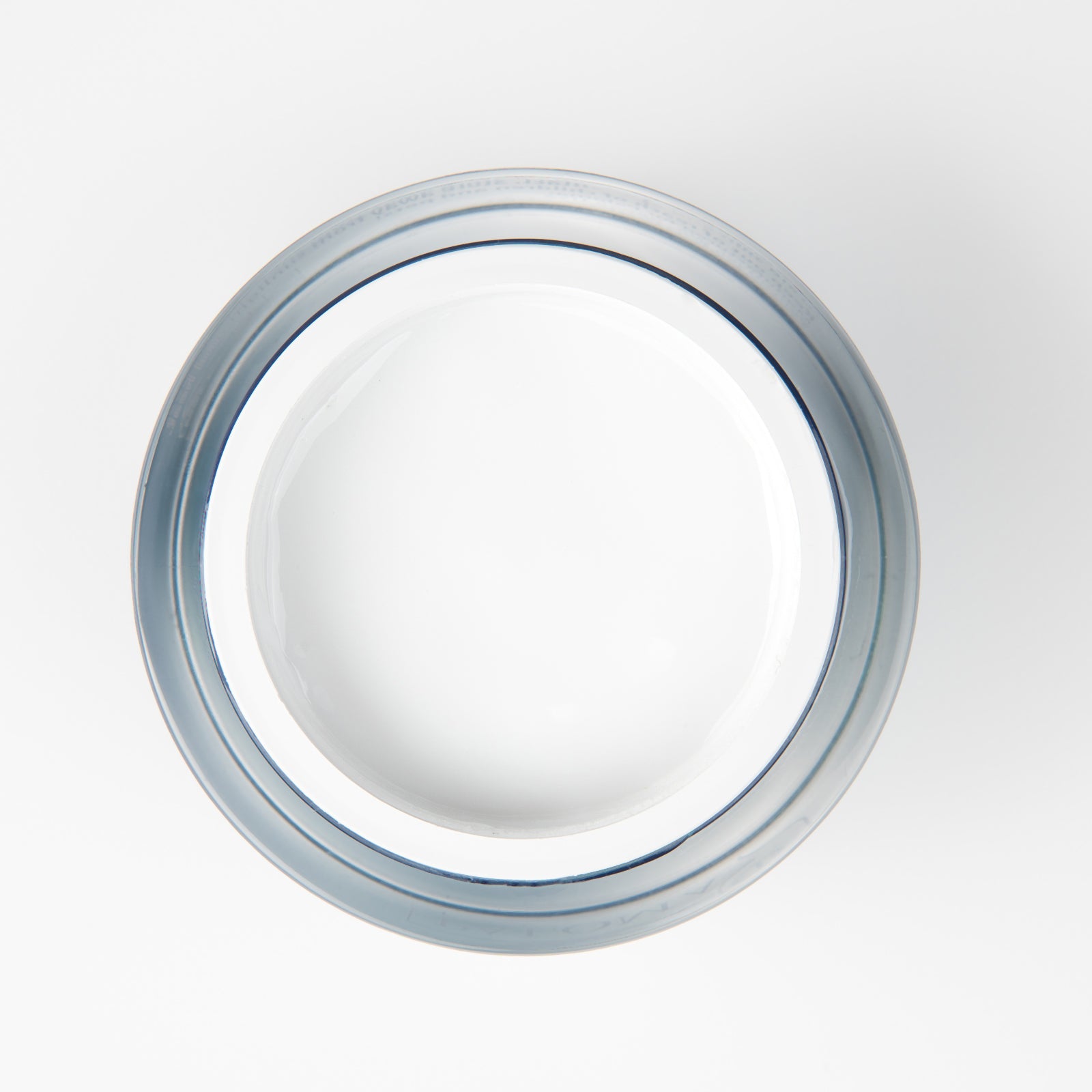 Top view of an open, transparent, circular jar filled with white builder gel, revealing a dense and creamy texture. The jar is placed against a pristine white backdrop, suggestive of a professional studio setting.